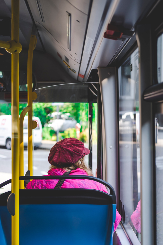 A person in a pink coat and beret looks out the window while riding the bus